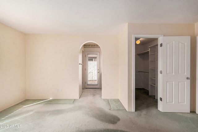 unfurnished bedroom featuring carpet flooring, a walk in closet, arched walkways, baseboards, and a closet