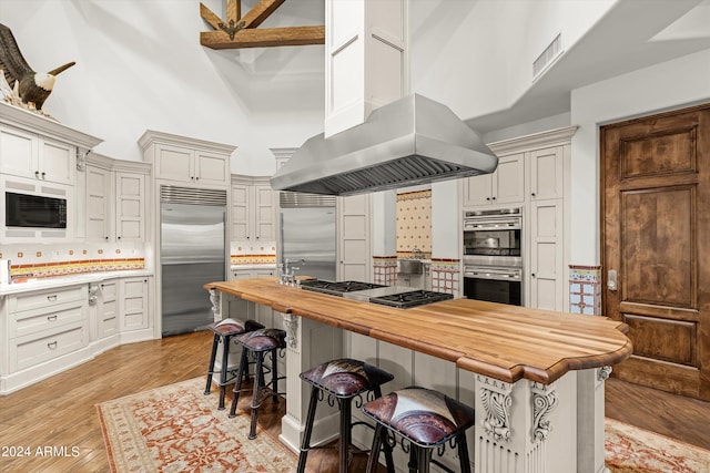 kitchen with high vaulted ceiling, light hardwood / wood-style floors, a breakfast bar, and built in appliances