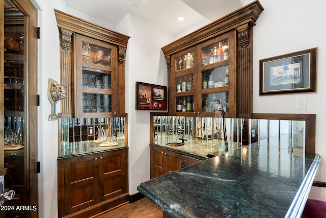 bar featuring stainless steel dishwasher, dark hardwood / wood-style flooring, sink, and dark stone counters