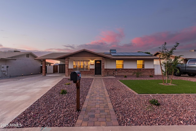 ranch-style house with brick siding, solar panels, and concrete driveway
