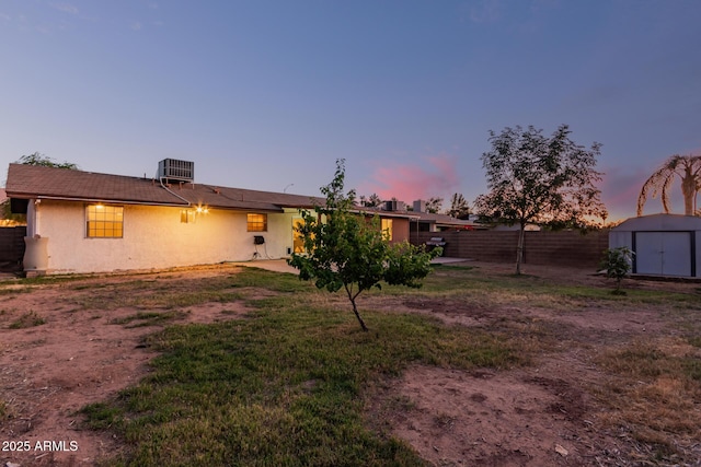 back of property at dusk featuring a shed, fence, an outdoor structure, stucco siding, and cooling unit