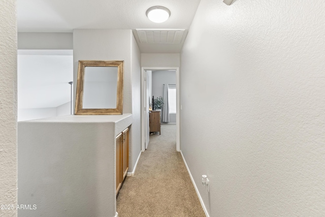 hall with baseboards, visible vents, a textured wall, and light carpet