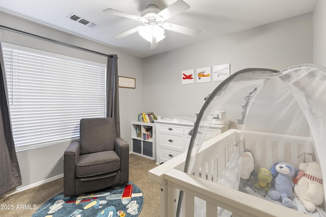 carpeted bedroom featuring a crib, a ceiling fan, visible vents, and baseboards