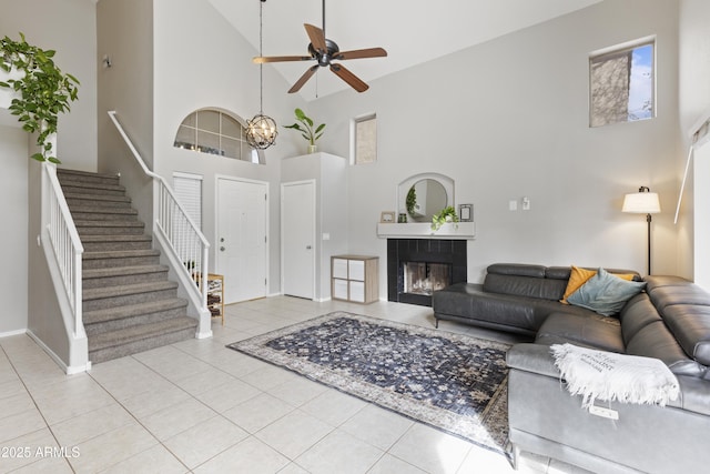 tiled living area with stairs, a towering ceiling, a fireplace, and ceiling fan with notable chandelier