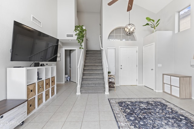 tiled entrance foyer with visible vents, high vaulted ceiling, stairs, and ceiling fan with notable chandelier