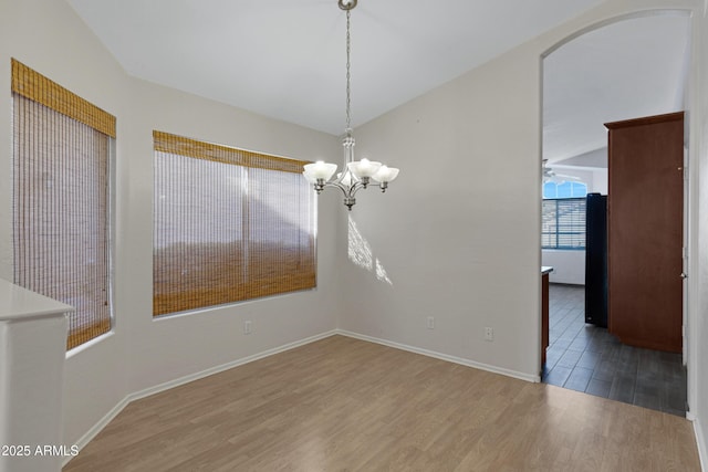 unfurnished dining area with hardwood / wood-style flooring, lofted ceiling, and a notable chandelier