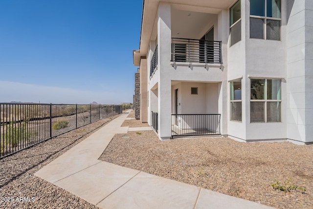 view of property exterior with a patio, fence, a balcony, and stucco siding