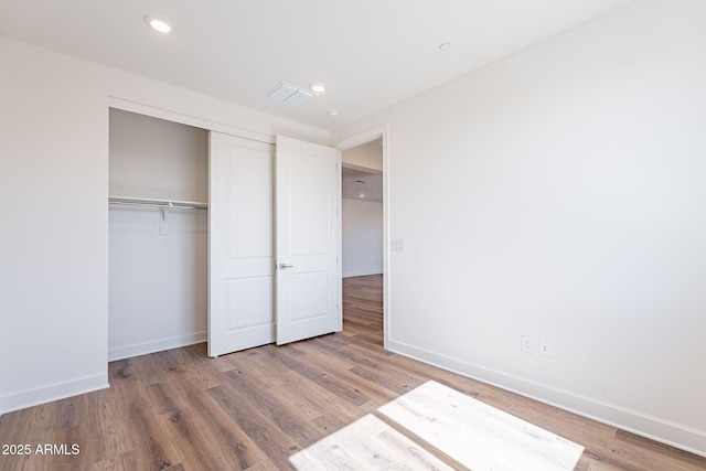 unfurnished bedroom featuring recessed lighting, wood finished floors, visible vents, baseboards, and a closet