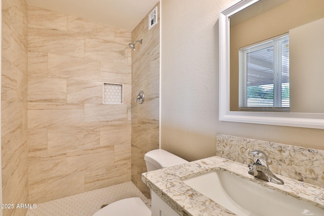 bathroom with vanity, toilet, and tiled shower