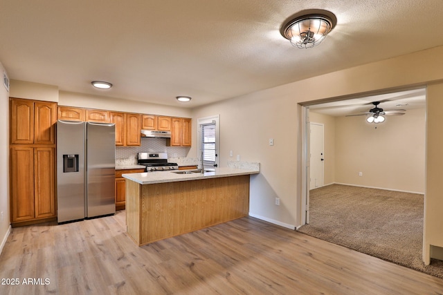 kitchen featuring sink, light wood-type flooring, kitchen peninsula, stainless steel appliances, and backsplash