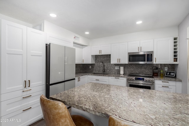 kitchen with a breakfast bar area, stainless steel appliances, a sink, white cabinetry, and tasteful backsplash