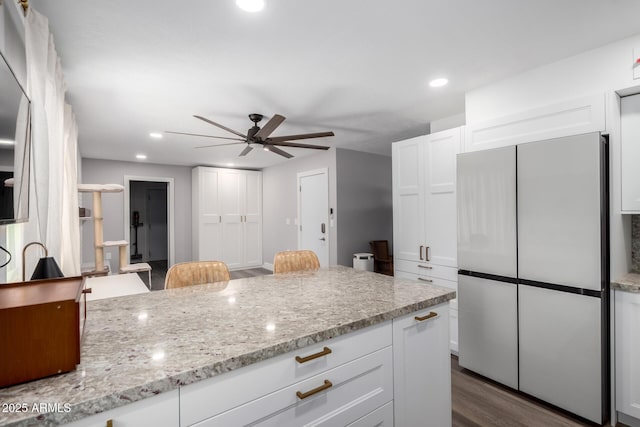 kitchen featuring white cabinets, ceiling fan, light stone counters, dark wood-type flooring, and freestanding refrigerator