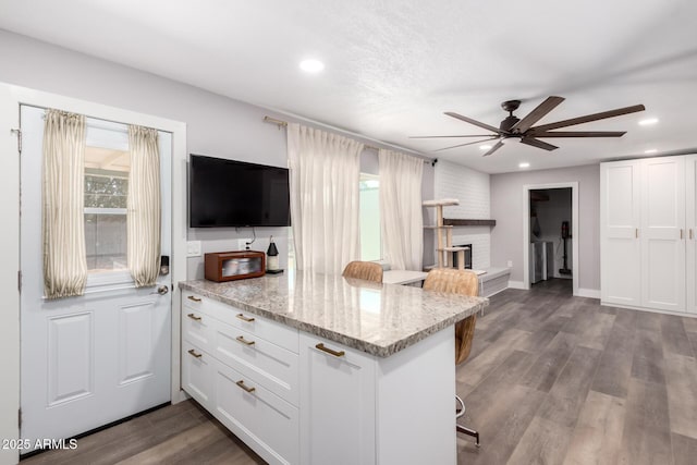 kitchen with dark wood-style floors, light stone counters, white cabinets, a peninsula, and a kitchen bar