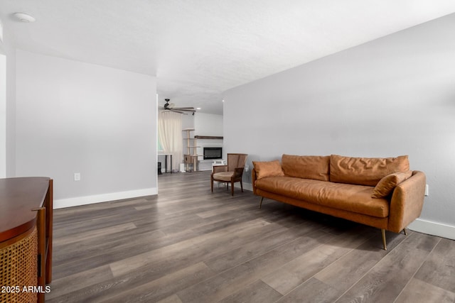 living area with a ceiling fan, a fireplace, baseboards, and wood finished floors