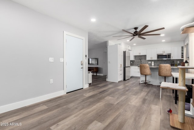 kitchen featuring stainless steel appliances, backsplash, white cabinets, wood finished floors, and a kitchen bar