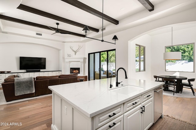 kitchen featuring an island with sink, hanging light fixtures, sink, white cabinetry, and light stone counters