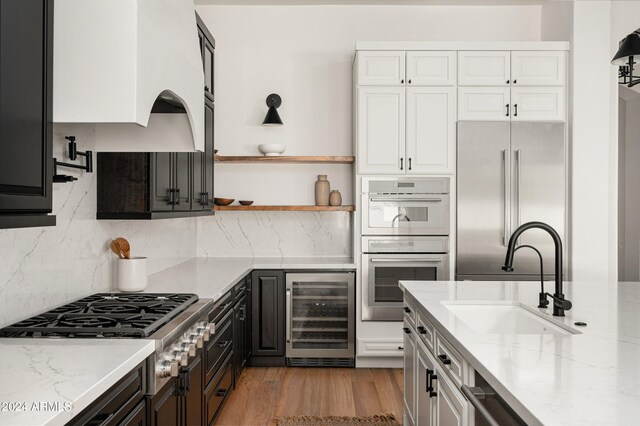 kitchen with appliances with stainless steel finishes, white cabinetry, light stone countertops, and beverage cooler