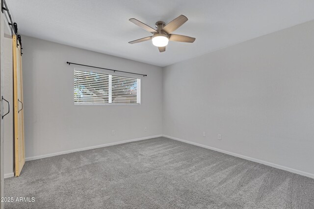 spare room featuring ceiling fan, a barn door, and carpet flooring