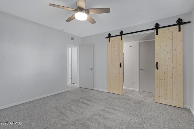 unfurnished bedroom featuring light carpet, ceiling fan, and a barn door