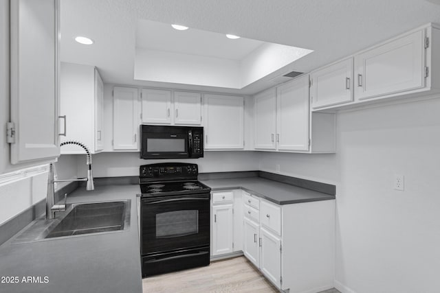 kitchen featuring a raised ceiling, black appliances, light hardwood / wood-style floors, sink, and white cabinetry