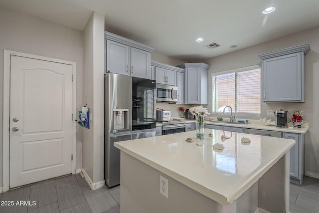 kitchen featuring stainless steel appliances, a kitchen island, sink, and gray cabinetry