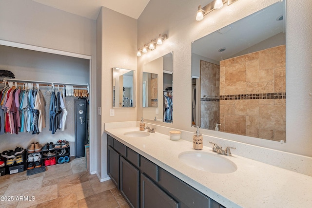 full bathroom featuring a spacious closet, double vanity, a sink, and stone tile flooring