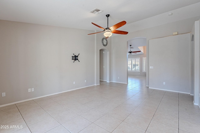 empty room featuring arched walkways, light tile patterned flooring, visible vents, baseboards, and a ceiling fan