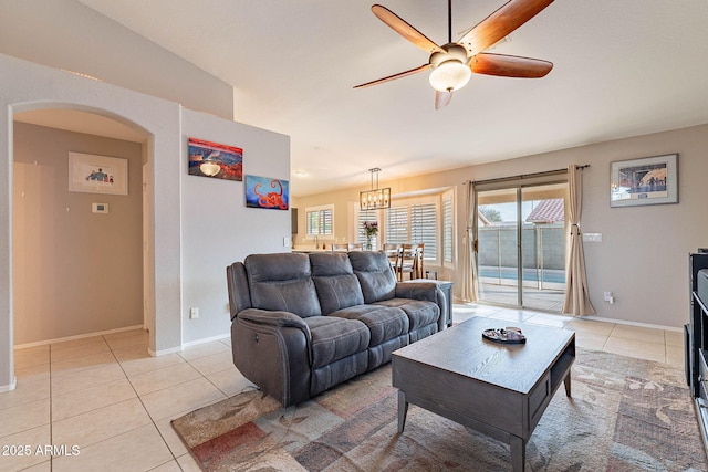 living room featuring light tile patterned floors, ceiling fan, arched walkways, and baseboards