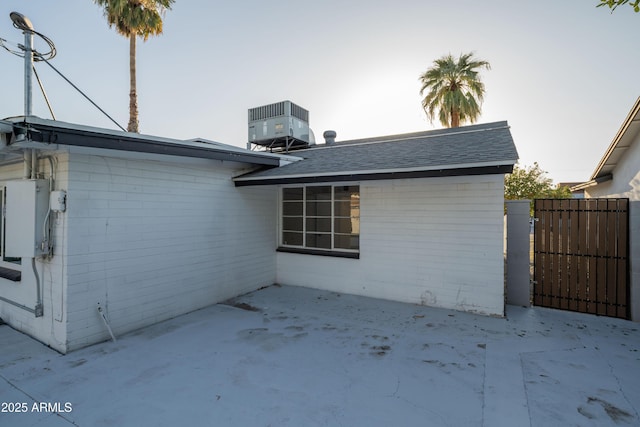 back of property featuring a patio, a gate, roof with shingles, central AC, and brick siding