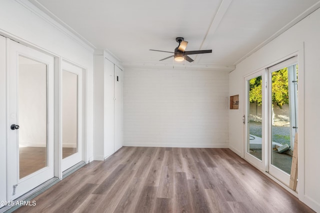 empty room featuring brick wall, crown molding, a ceiling fan, and wood finished floors