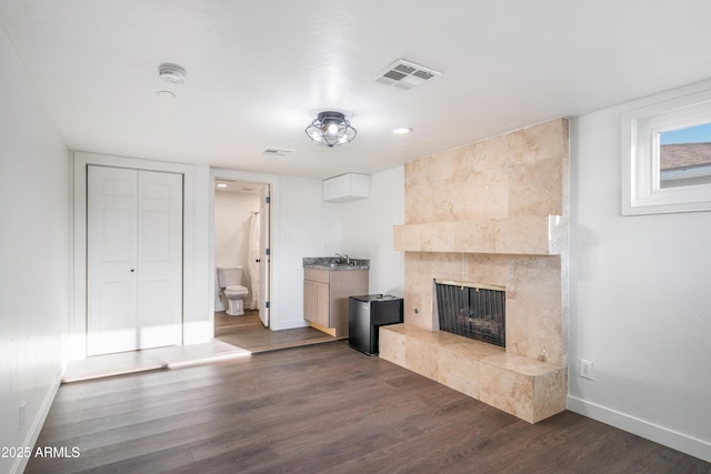 unfurnished living room featuring baseboards, visible vents, dark wood-style flooring, and a tile fireplace