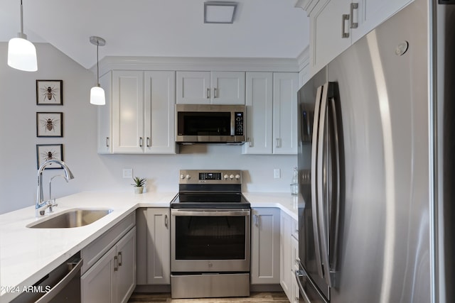 kitchen with light wood-type flooring, light stone counters, stainless steel appliances, sink, and hanging light fixtures