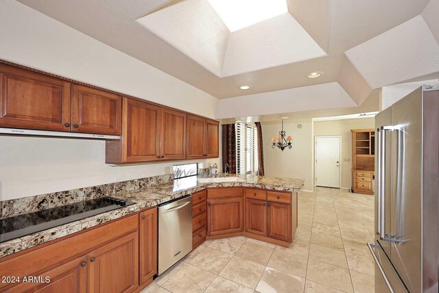 kitchen with light tile patterned flooring, kitchen peninsula, a raised ceiling, appliances with stainless steel finishes, and decorative light fixtures