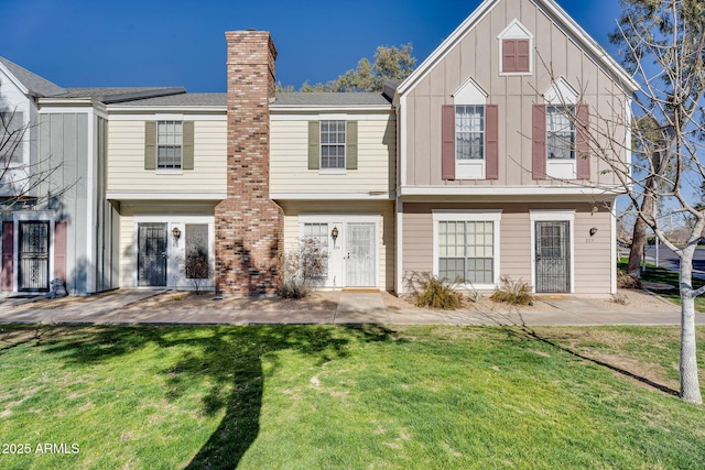 back of property featuring board and batten siding, a patio area, a chimney, and a lawn