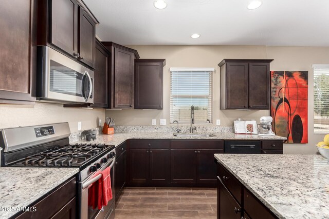 kitchen featuring light stone countertops, a sink, dark brown cabinets, and stainless steel appliances