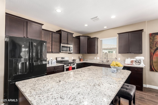kitchen featuring dark brown cabinets, visible vents, a kitchen island, appliances with stainless steel finishes, and a sink