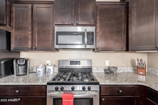 kitchen featuring appliances with stainless steel finishes, dark brown cabinets, and light stone countertops