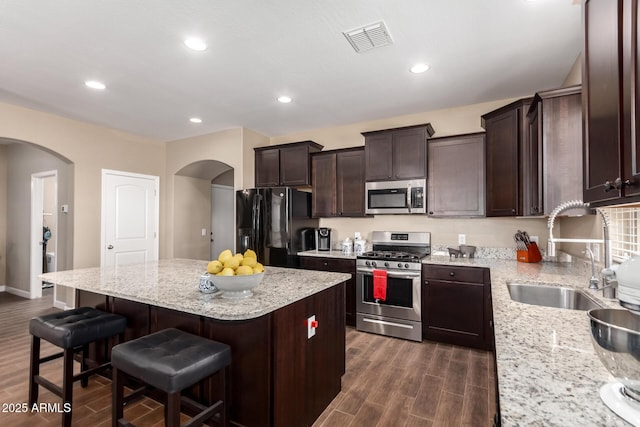 kitchen with arched walkways, visible vents, a sink, stainless steel appliances, and dark wood-style floors