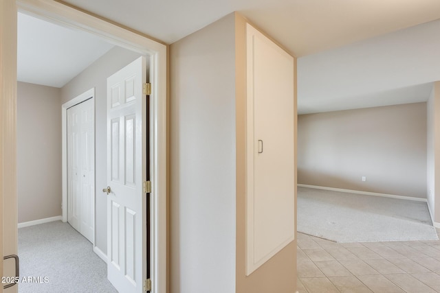 hallway with light colored carpet, baseboards, and light tile patterned flooring