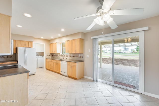 kitchen with a sink, light brown cabinetry, white appliances, and washing machine and clothes dryer