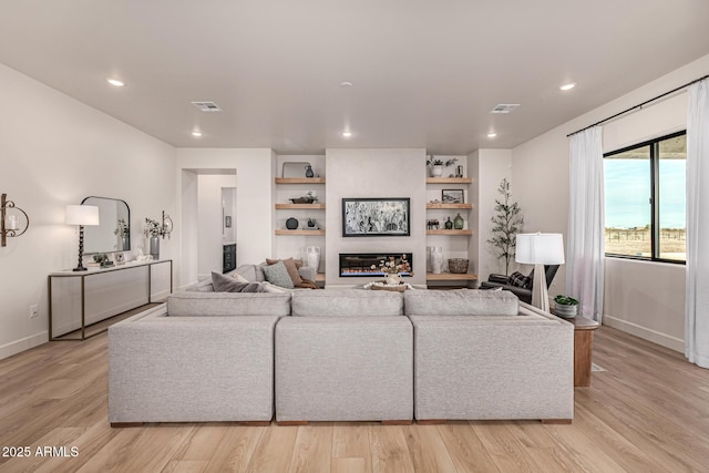 living room featuring a fireplace, light wood-type flooring, and built in shelves