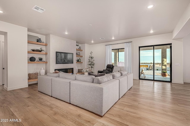 living room featuring a large fireplace, light wood-type flooring, and built in shelves