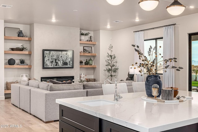 kitchen with light stone countertops, a kitchen island with sink, built in features, and light hardwood / wood-style flooring