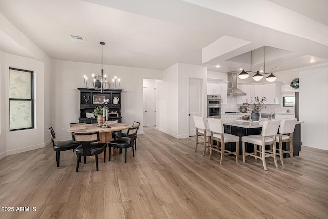 dining area with a tray ceiling, light hardwood / wood-style flooring, and a notable chandelier