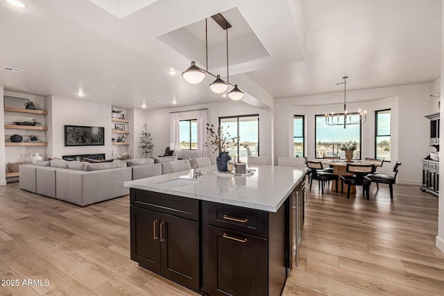 kitchen featuring sink, light hardwood / wood-style floors, light stone countertops, a kitchen island, and decorative light fixtures