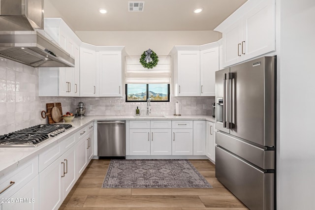 kitchen featuring range hood, white cabinetry, sink, backsplash, and stainless steel appliances