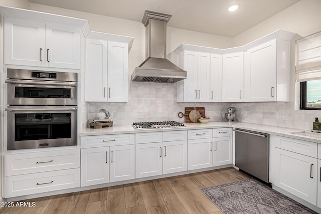 kitchen featuring white cabinetry, appliances with stainless steel finishes, wall chimney range hood, and backsplash