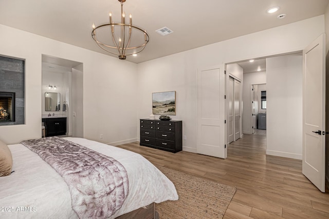 bedroom featuring connected bathroom, an inviting chandelier, a closet, a fireplace, and hardwood / wood-style floors