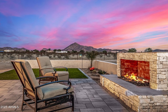 patio terrace at dusk with a mountain view and an outdoor stone fireplace