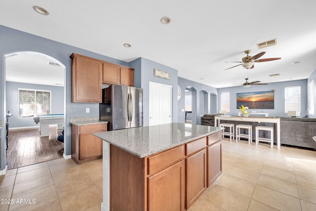 kitchen featuring light stone countertops, a center island, pool table, stainless steel fridge, and light tile patterned floors